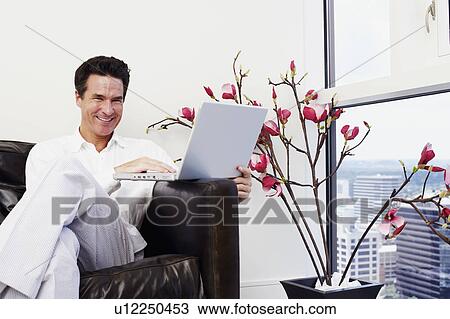 Portrait of a mature man sitting on a couch and using a laptop View Large Photo Image Stock Image - Portrait of a mature man sitting on a couch and using a laptop. Fotosearch