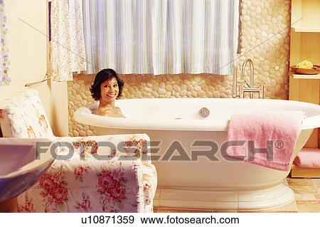 Stock Photo - Portrait of a mature woman sitting in a bathtub and smiling. Fotosearch