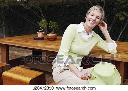 Stock Image - Portrait of a mature woman sitting on a stool and smiling. Fotosearch