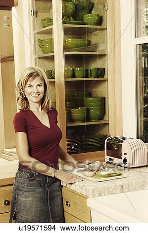 Picture - Portrait of a mature woman standing in the kitchen and smiling. Fotosearch