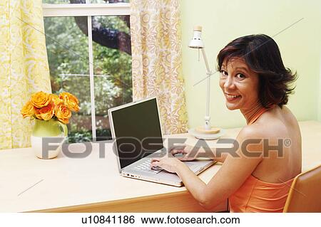 Stock Photograph - Portrait of a mature woman using a laptop and smiling. Fotosearch