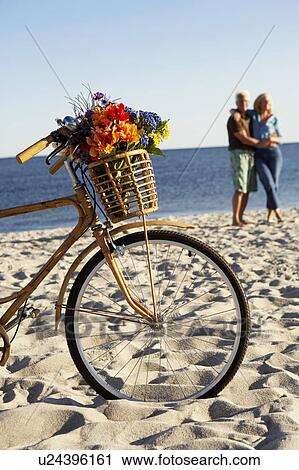 Stock Image - Close-up of a bicycle with a mature couple standing in the background. Fotosearch