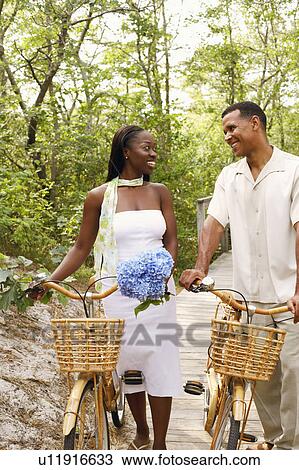 Couple standing with bicycles on a boardwalk and smiling View Large Photo Image Stock Image - Couple standing with bicycles on a boardwalk and smiling. Fotosearch