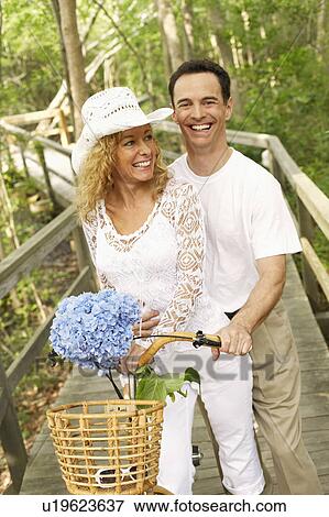 Stock Photo - Mature couple standing with a bicycle and smiling. Fotosearch