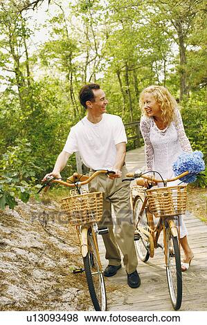 Stock Photo - Mature couple walking on a boardwalk with bicycles. Fotosearch
