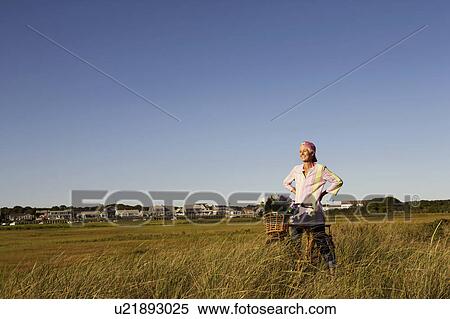 Stock Photography - Mature woman standing in a field with a bicycle. Fotosearch