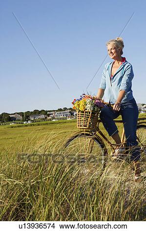 Picture - Mature woman standing in the field with a bicycle. Fotosearch