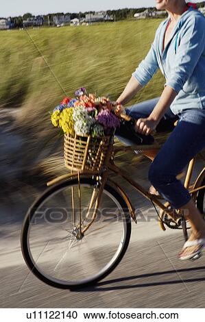 Stock Image - Mid section view of a woman carrying flowers in a basket on her bicycle. Fotosearch