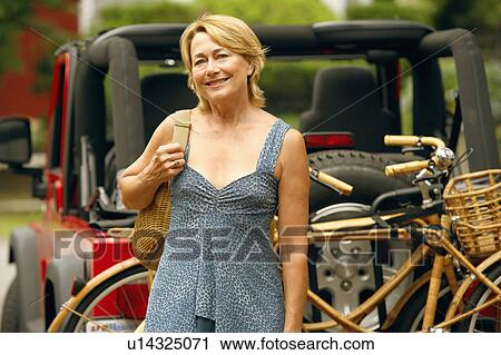 Stock Image - Portrait of a mature woman smiling with a sports utility vehicle and bicycles in the background. Fotosearch