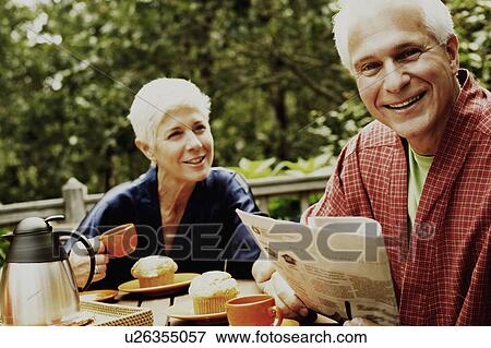 Stock Photo - Close-up of a mature man and a senior woman sitting at the table and smiling. Fotosearch