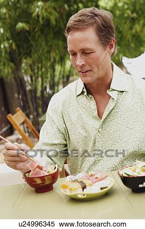 Stock Photography - Close-up of a mature man eating with chopsticks. Fotosearch