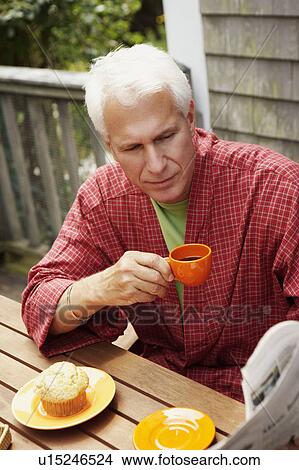 Close-up of a mature man sitting at the table and holding a cup of black tea View Large Photo Image Picture - Close-up of a mature man sitting at the table and holding a cup of black tea. Fotosearch