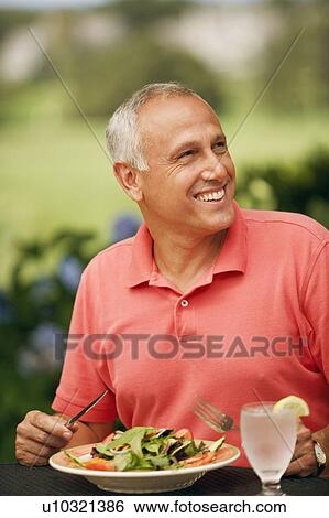 Stock Photograph - Close-up of a mature man sitting at the table with a plate of vegetable salad in front of him. Fotosearch