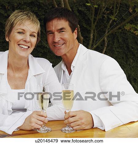 Mature couple holding champagne flutes and smiling View Large Photo Image Stock Photo - Mature couple holding champagne flutes and smiling. Fotosearch