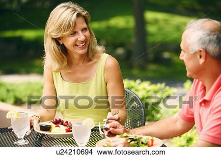 Picture - Mature couple sitting at the table with plates of salad in front of them. Fotosearch