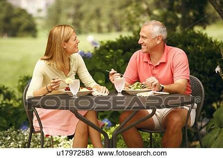 Stock Image - Mature man with a mid adult woman sitting at the table with plates of salad in front of them. Fotosearch