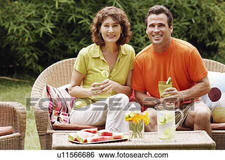 Stock Photograph - Portrait of a mature couple sitting on a couch and holding glasses of lemonade. Fotosearch