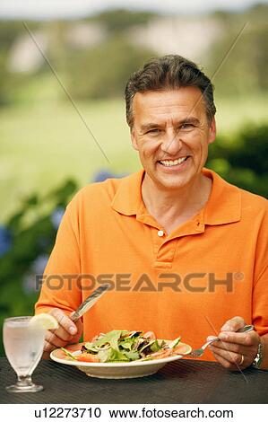 Stock Image - Portrait of a mature man sitting at the table with a plate of vegetable salad in front of him. Fotosearch