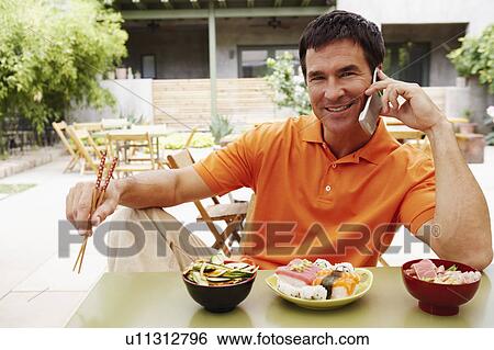 Stock Photograph - Portrait of a mature man sitting at the table and talking on a mobile phone. Fotosearch