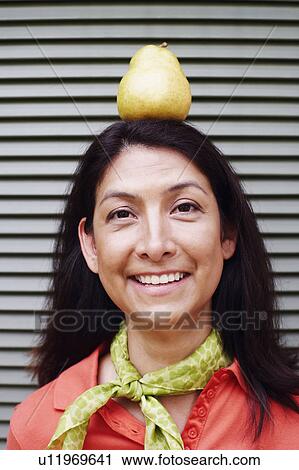 Stock Image - Portrait of a mature woman balancing a pear on her head. Fotosearch