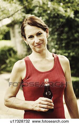 Stock Image - Portrait of a mature woman holding a bottle of wine and smiling. Fotosearch