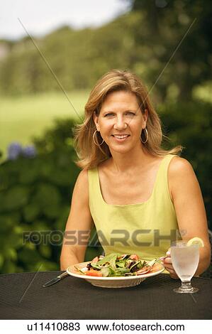 Stock Image - Portrait of a mature woman sitting at the table with a plate of vegetable salad in front of her. Fotosearch