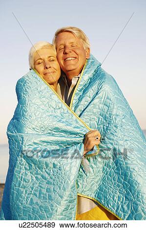 Stock Photo - Close-up of a mature couple wrapped in a blanket and smiling. Fotosearch