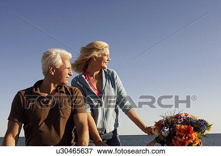 Stock Photo - Mature couple with a bicycle on the beach. Fotosearch