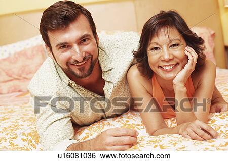 Stock Photograph - Portrait of a mature couple lying on the bed and smiling. Fotosearch