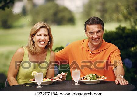 Picture - Portrait of a mature couple sitting at the table with plates of salad in front of them. Fotosearch