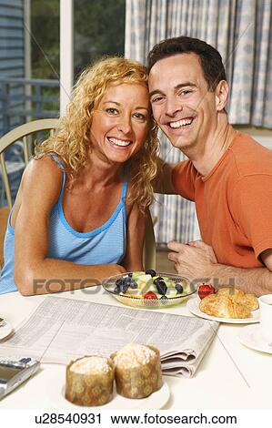 Stock Image - Portrait of a mature couple sitting at the breakfast table and smiling. Fotosearch