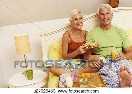 Stock Image - Portrait of a mature man and a senior woman having breakfast in bed. Fotosearch