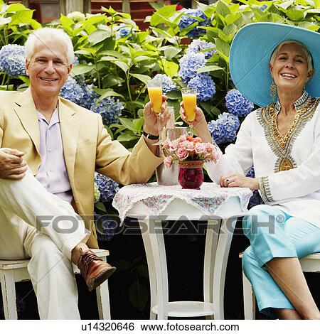 Stock Photograph - Portrait of a mature man and a senior woman sitting together and holding glasses of juice. Fotosearch