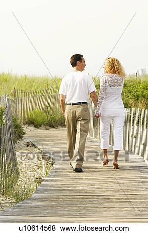 Stock Photo - Rear view of a man and a woman walking on a boardwalk. Fotosearch
