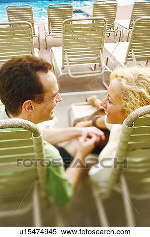 Stock Photography - Rear view of a mature couple reclining on lounge chairs. Fotosearch