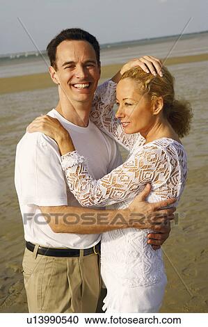 Stock Image - Side profile of a mature couple embracing each other on the beach. Fotosearch