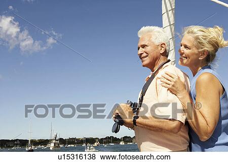Side profile of a mature man holding a pair of binoculars with a mature woman standing behind him View Large Photo Image Stock Photo - Side profile of a mature man holding a pair of binoculars with a mature woman standing behind him. Fotosearch
