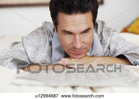 Stock Photo - Close-up of a mature man lying on the bed and reading a newspaper. Fotosearch