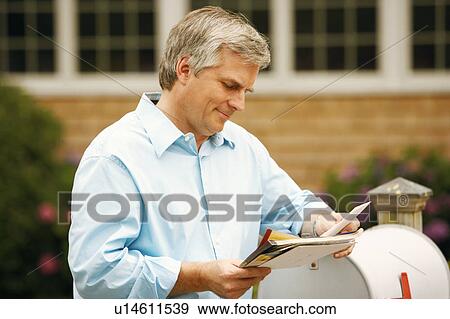 Stock Photo - Close-up of a mature man reading mail near a mailbox. Fotosearch
