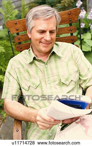 Stock Photo - Close-up of a mature man sitting on a chair and reading a book. Fotosearch