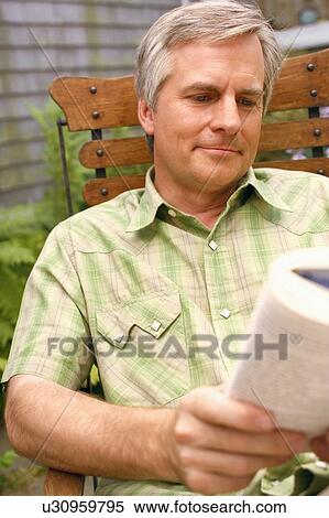 Stock Photography - Close-up of a mature man sitting on a chair and reading a book. Fotosearch