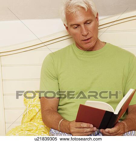 Stock Photography - Close-up of a mature man sitting on the bed and reading a book. Fotosearch