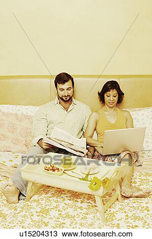 Mature man reading a newspaper with a mature woman using a laptop on the bed View Large Photo Image Stock Image - Mature man reading a newspaper with a mature woman using a laptop on the bed. Fotosearch
