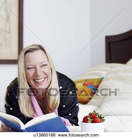 Mature woman lying on the bed with a book and smiling View Large Photo Image Stock Photo - Mature woman lying on the bed with a book and smiling. Fotosearch
