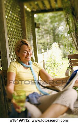 Mature woman sitting on a chair and reading a magazine View Large Photo Image Stock Image - Mature woman sitting on a chair and reading a magazine. Fotosearch