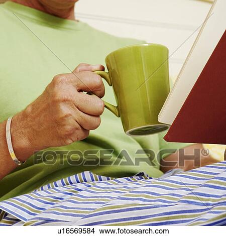 Picture - Mid section view of a man holding a book and a mug. Fotosearch