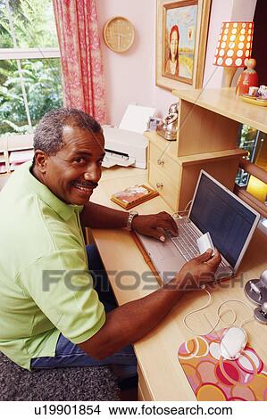 Picture - Portrait of a mature man holding a credit card and using a laptop. Fotosearch