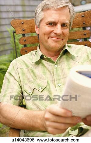 Stock Photograph - Portrait of a mature man sitting on a chair and holding a book. Fotosearch