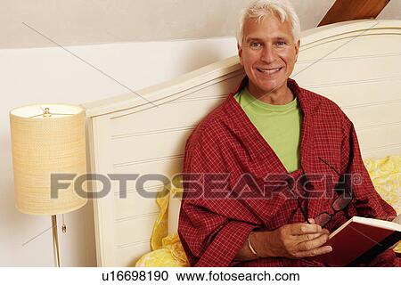 Stock Image - Portrait of a mature man sitting on the bed and smiling. Fotosearch