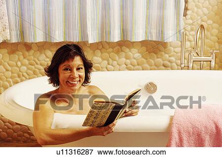 Stock Photo - Portrait of a mature woman sitting in a bathtub holding a book. Fotosearch